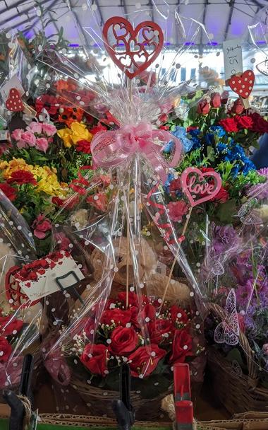 Red roses and a teddy with other flower arrangements in the background